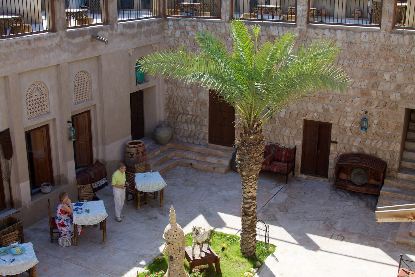 A courtyard in the Al Fahidi quarter: coral-stone walls, carved window screens, a date palm and low tables in the shade.