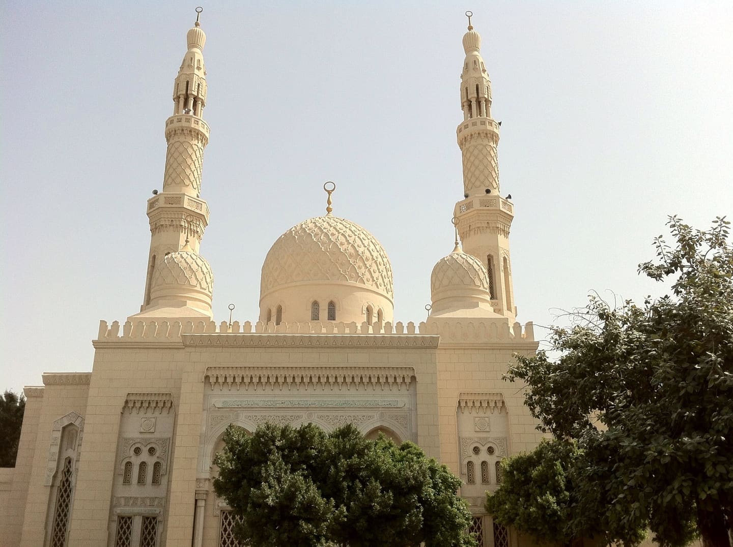 The pale stone facade of Jumeirah Mosque: a central ribbed dome flanked by two tall minarets against a clear sky.
