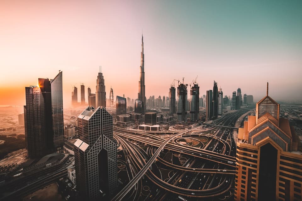 Dubai at dusk from above: the Sheikh Zayed Road interchange sweeping between the towers, traffic on every carriageway, the Burj Khalifa at the centre of the skyline.
