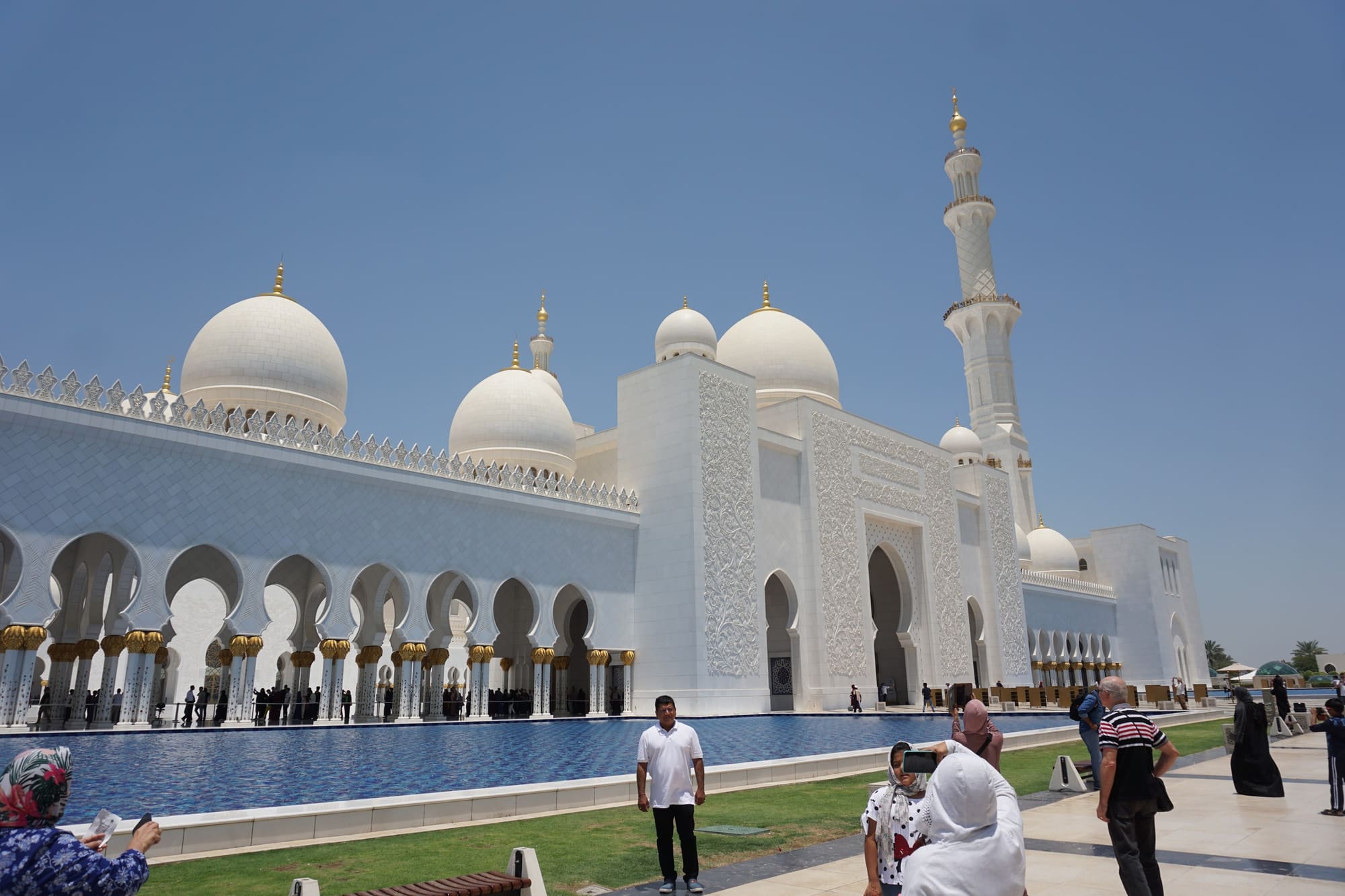 Visitors in the sunlit courtyard of Sheikh Zayed Grand Mosque